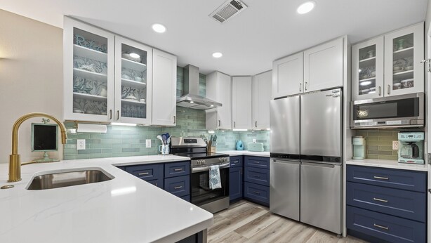 Een moderne keuken met witte en blauwe kastjes, roestvrijstalen apparatuur en een marmeren aanrecht.