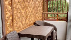Un balcon agrémenté de meubles en osier, d’un mur en fibres tressées et offrant une vue sur la verdure.