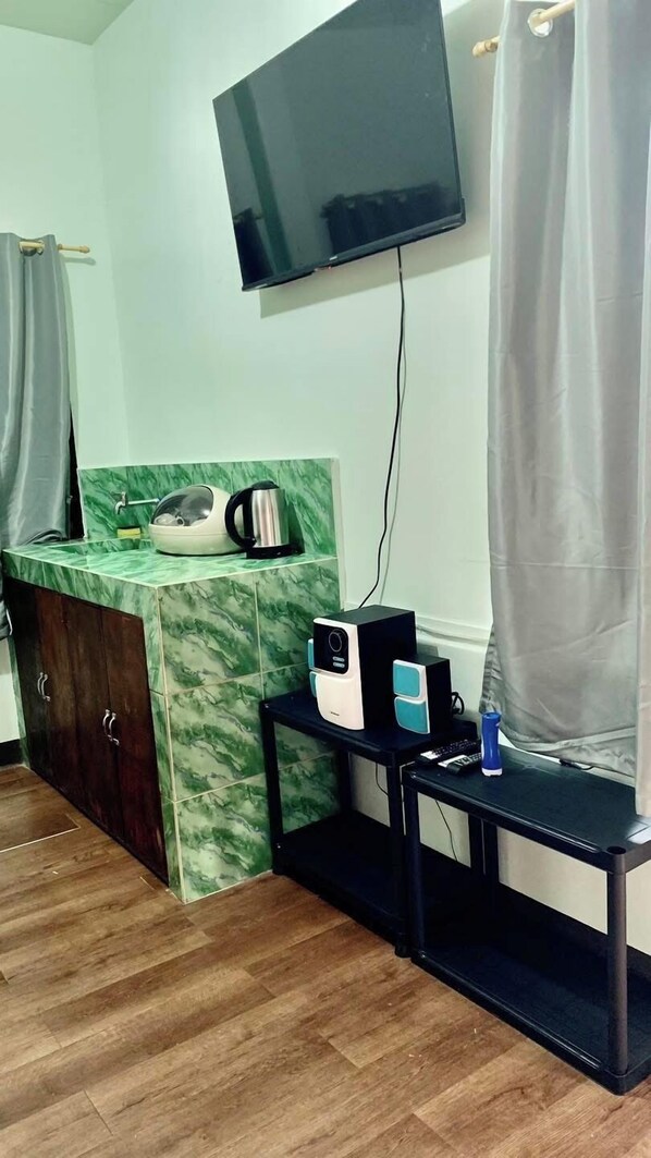 Une pièce dotée d’un téléviseur fixé au mur, d’une petite table avec une bouilloire et une machine à café, d’un meuble avec un plan de travail en marbre et d’un plancher en bois.