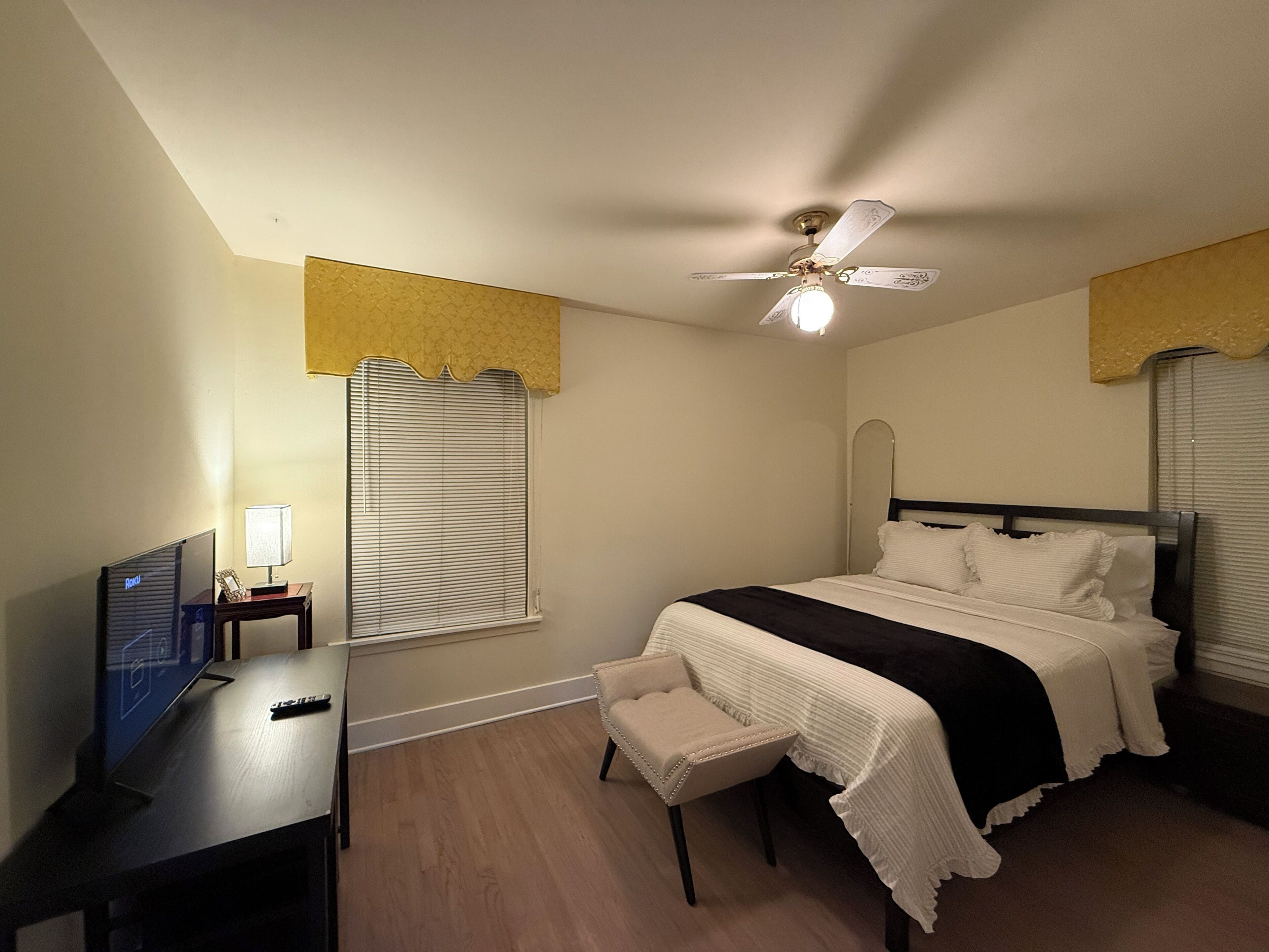 A bedroom with a bed, bedside table, lamp, and ceiling fan.