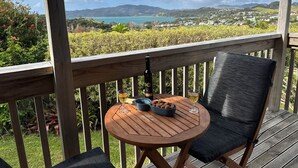 En træterrasse med et rundt bord og to stole, med udsigt over et naturskønt landskab med bakker og et vandareal.