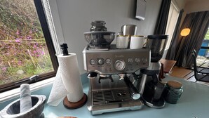 A kitchen with a coffee machine, a wooden cutting board, a mortar and pestle, and a window with a view of flowers. - Casa Playa de los osos | Coopers Beach Sea Views (Cable Bay)