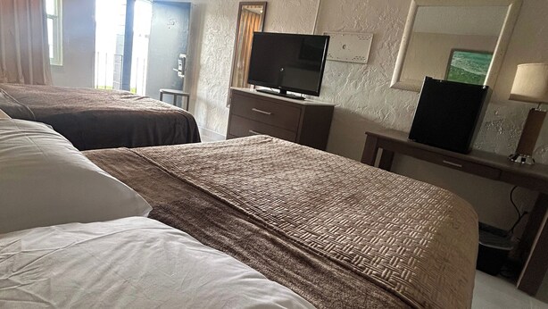 A hotel room with two beds, a television, a desk, and a mirror. - Gardenview (Tampa)