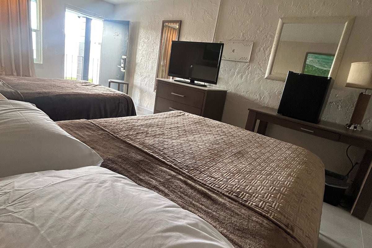 A hotel room with two beds, a television, a desk, and a mirror.
