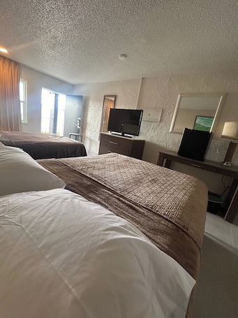 A hotel room with two beds, a television, a desk, and a mirror.