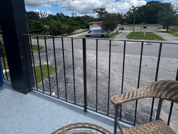 A balcony with a wicker chair, a view of a parking lot, and a building in the background. - Gardenview (Tampa)