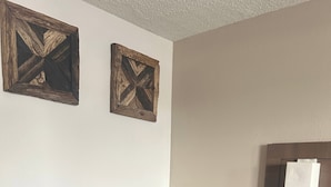 A room with a sofa, a bedside table, a mirror, and two wall-mounted picture frames. - Gardenview (Tampa)