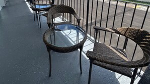 A balcony with wicker chairs and a glass table. - Gardenview (Tampa)