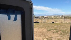A view from inside a camper with a window, looking out at a fenced field with a clear sky. - Cozy 2-bedroom RV in enchanting Carrizozo with AC on 5.5 acres! (Carrizozo)