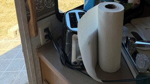 A window with a view of a grassy field, a blue container, and a roll of toilet paper on a counter. - Cozy 2-bedroom RV in enchanting Carrizozo with AC on 5.5 acres! (Carrizozo)