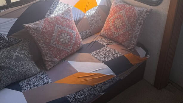 A bed with patterned pillows and a geometric headboard in a room with a window and a view of the outside. - Cozy 2-bedroom RV in enchanting Carrizozo with AC on 5.5 acres! (Carrizozo)