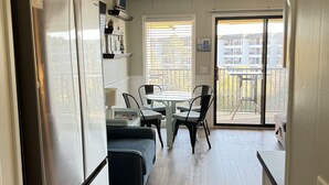A compact kitchen with a refrigerator, a dining area with a table and chairs, and a view through a window to an outdoor balcony. - Beach Front with Ocean View (Hilton Head Island)