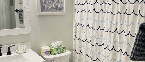 A bathroom with a toilet, sink, and mirror. There is a shower curtain with a wave pattern.