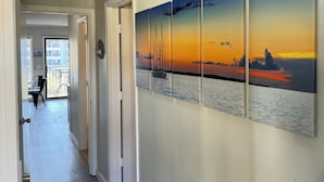 A hallway with a wooden floor, white walls, and a series of paintings depicting a sunset over water. - Beach Front with Ocean View (Hilton Head Island)
