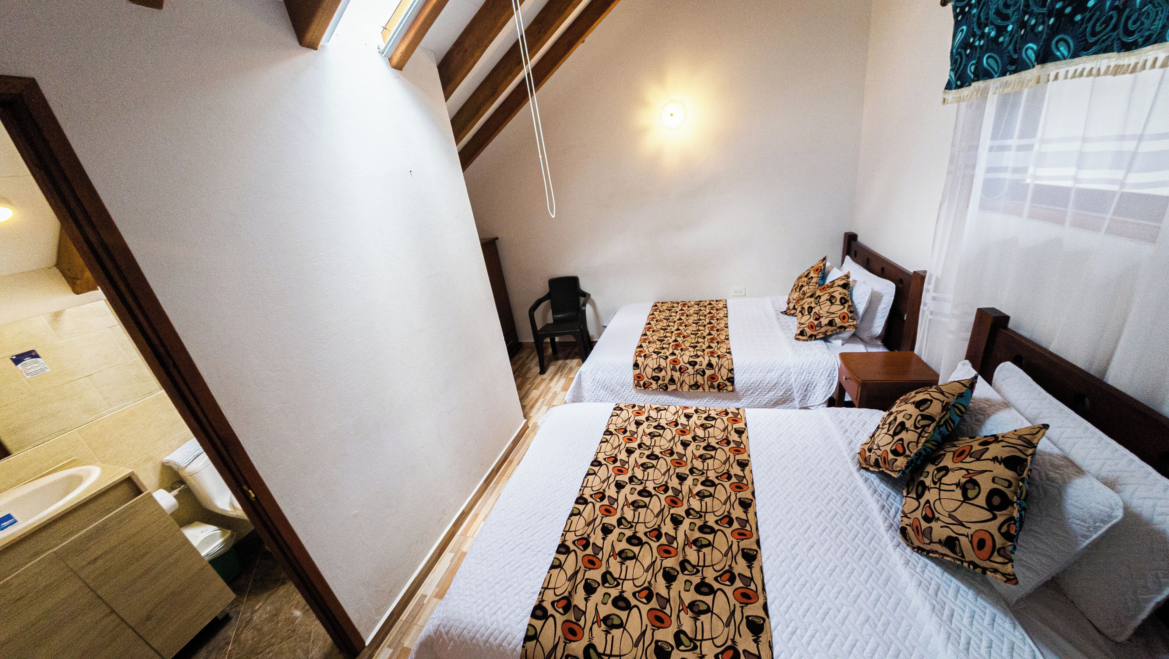 A hotel room with two beds, a wooden ceiling, a small table, and a chair.