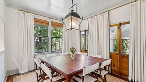 Une salle à manger avec une grande table en bois, des chaises à revêtement blanc et un luminaire suspendu.