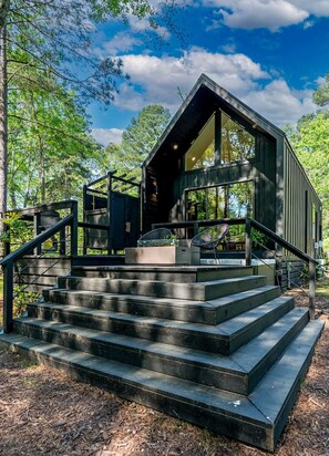 A modern cabin with a large glass window, surrounded by a forest.
