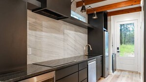 A modern kitchen with dark cabinetry, a marble backsplash, and wooden beams on the ceiling. - Private Lakeside Couples Cabin, Hot Tub & Fire Pit (Bullard)