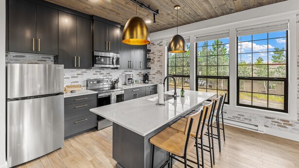 A modern kitchen with dark cabinets, stainless steel appliances, and a large island with bar stools. - The Loft 7- Steps from the Lake & Dining- Newly renovated in the heart of McCall (McCall)