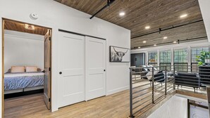 A modern interior with a wooden ceiling, a bed with a blue and white bedspread, a white door, and a staircase leading to an upper level. - The Loft 7- Steps from the Lake & Dining- Newly renovated in the heart of McCall (McCall)