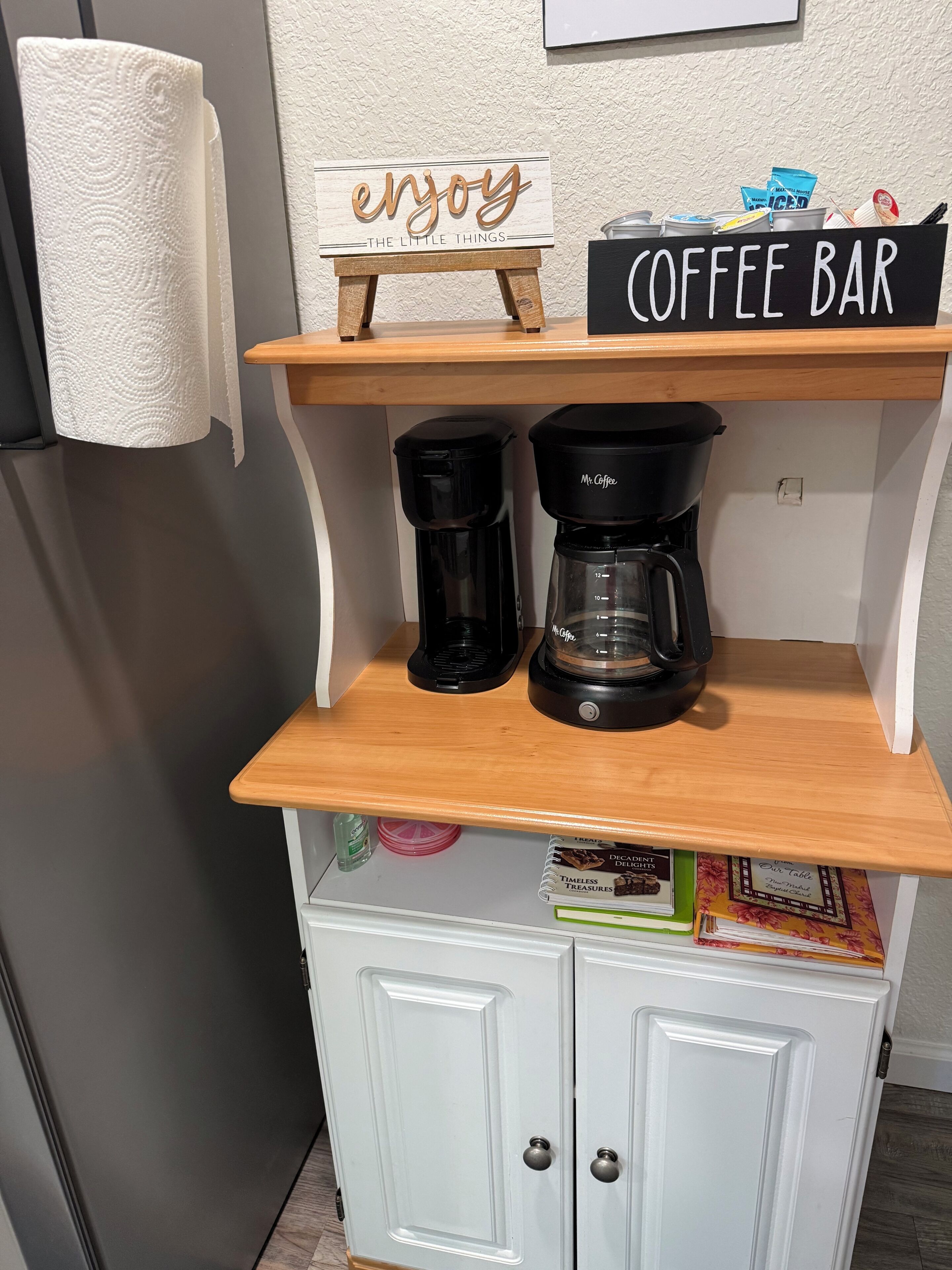 Een keukenhoek met een koffiebar, twee koffiezetapparaten, een bordje met de tekst 'geniet van de kleine dingen' en een bordje met de tekst 'COFFEE BAR'.