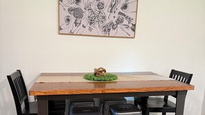 Una mesa de comedor con superficie de madera y patas de metal negro, rodeada por cuatro sillas negras.
