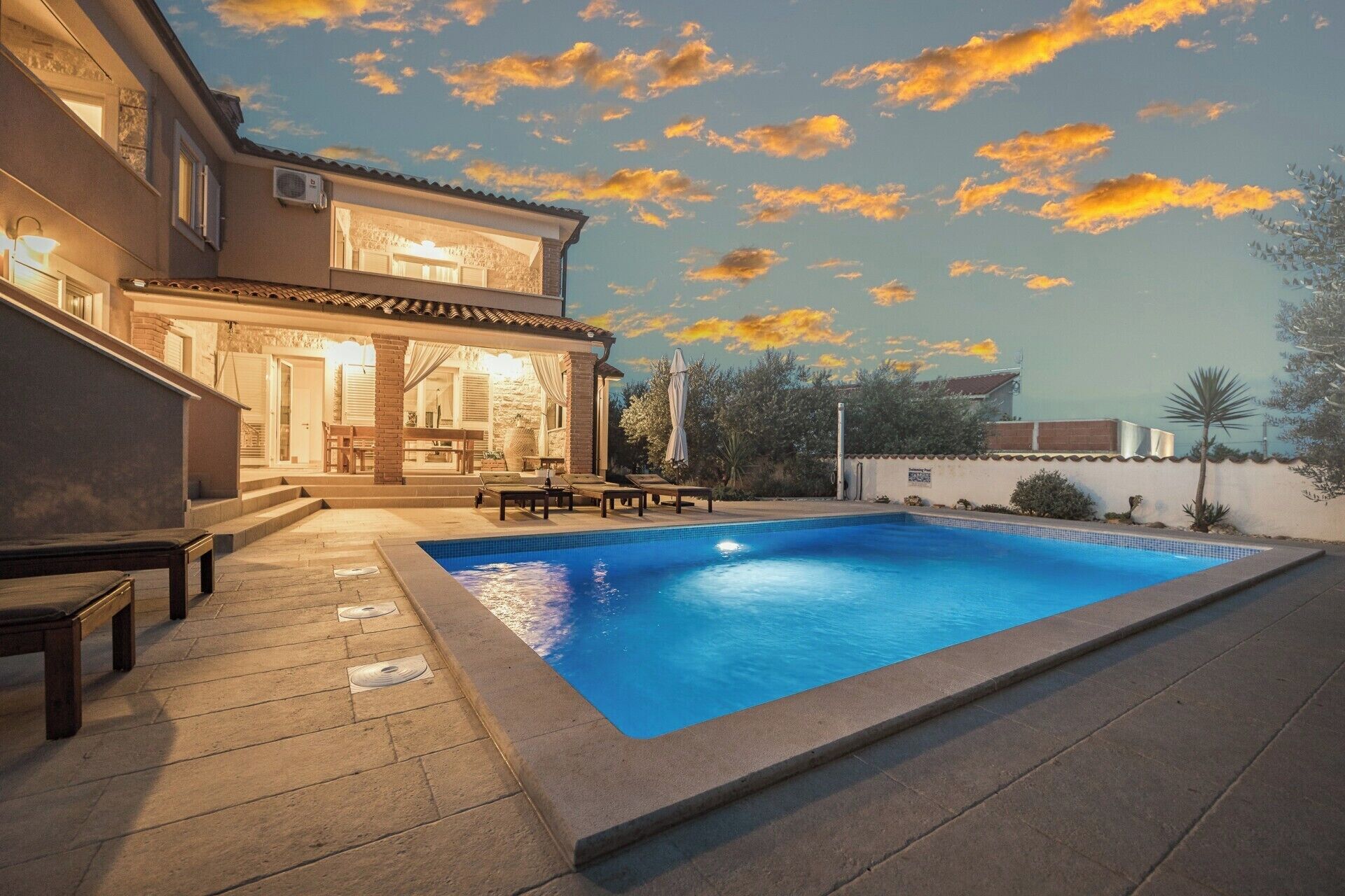 A swimming pool with a patio area, a covered outdoor seating area, and a building with a stone facade.