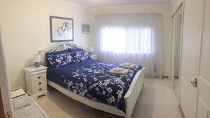 A neatly arranged bedroom with a bed, bedside tables, a lamp, and a window with curtains.