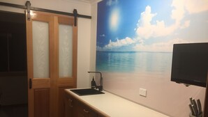 A kitchen with a wooden cabinet, a white countertop, a black faucet, and a wall-mounted television.