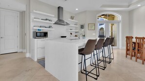 Una cocina moderna con armarios blancos, una isla central con taburetes, y un comedor con sillas de madera.