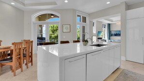 Una cocina moderna con una isla grande, armarios blancos y un comedor con sillas de madera.