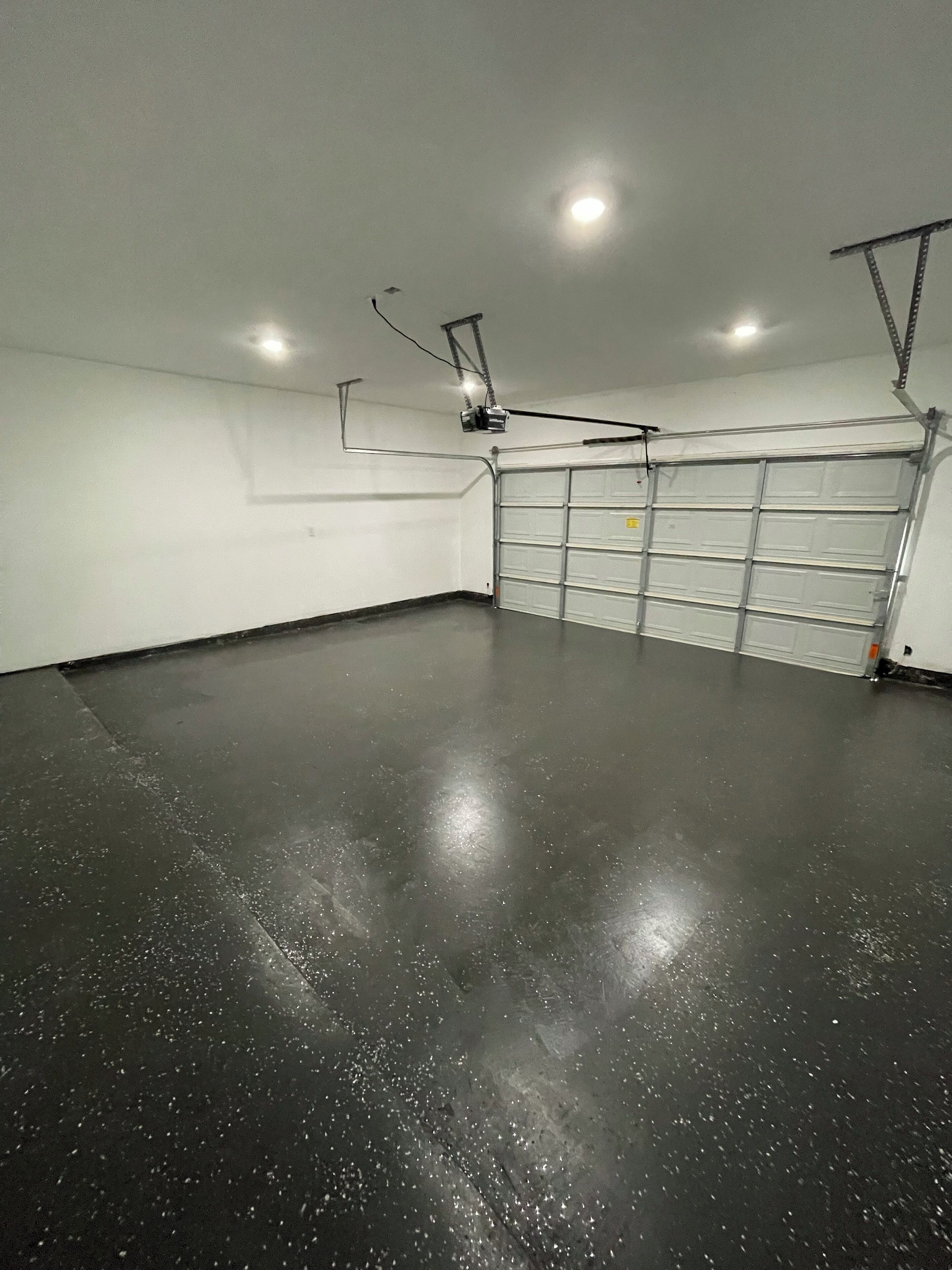 Un grand garage doté d’un sol en béton, d’une porte de garage blanche et d’un éclairage au plafond.