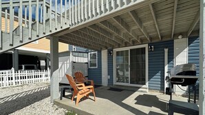 Un patio couvert avec une chaise en bois, un barbecue et une clôture blanche.