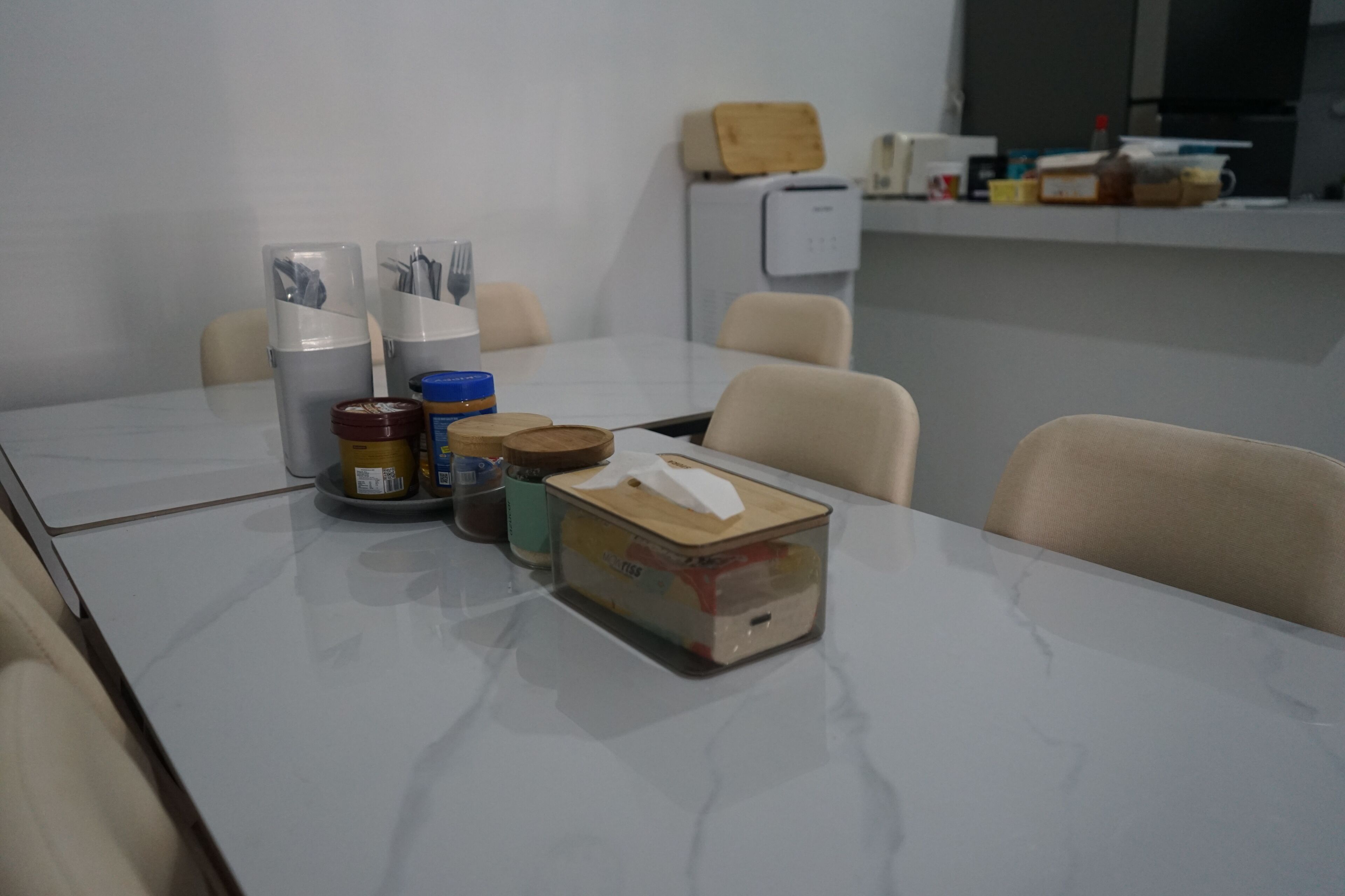 Une salle de conférence avec une table blanche, des chaises et divers objets, comme une machine à café, des bocaux et une boîte.