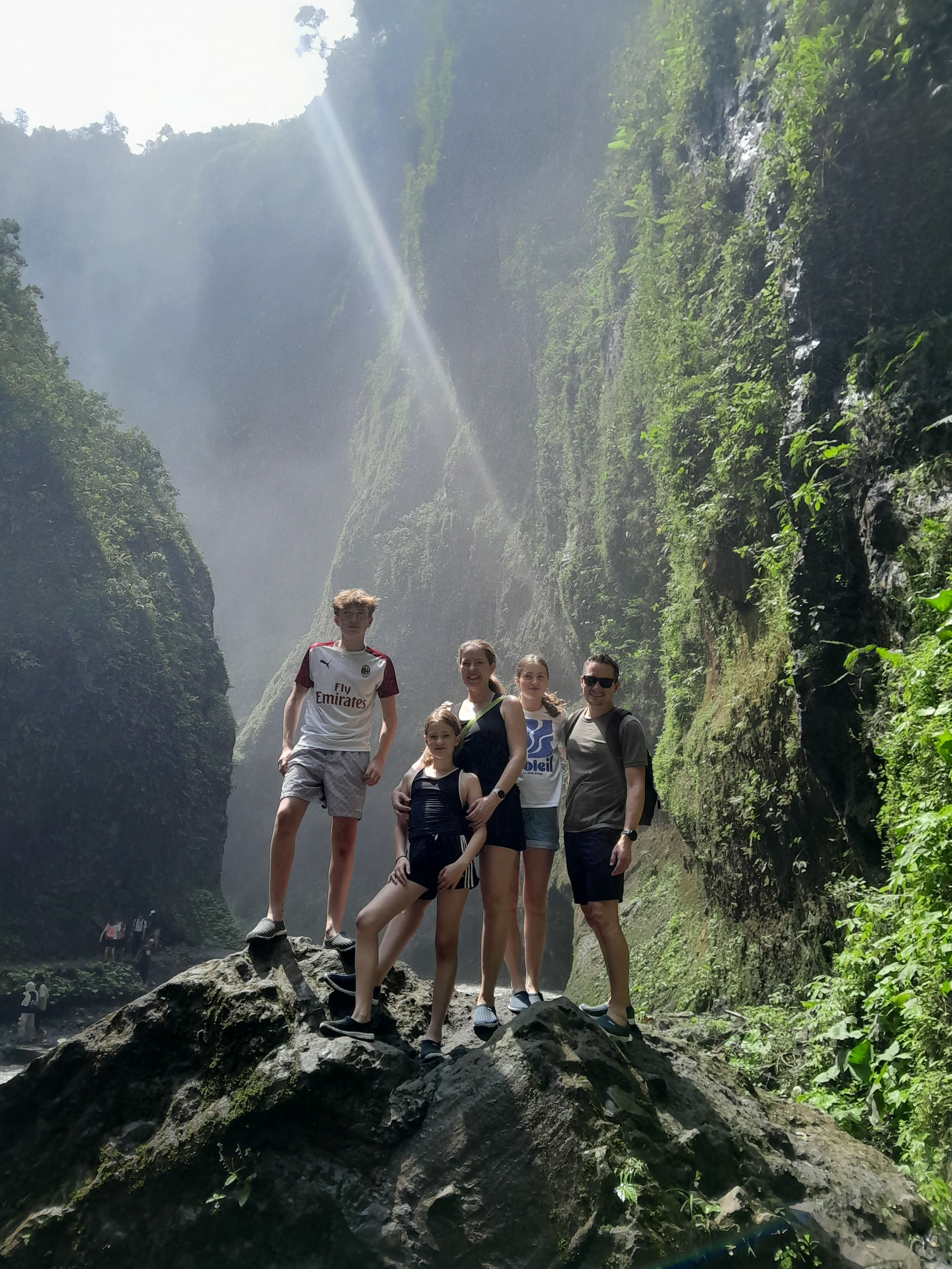 A group of people standing on a rocky outcrop with a mountainous landscape in the background.