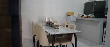 A modern kitchen with a dining table and chairs, a clock on the wall, and a refrigerator.