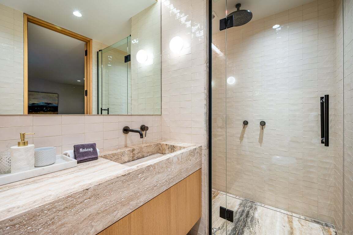 A bathroom with a marble sink, a large mirror, a glass shower enclosure, and a towel rack.