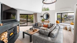 Una sala de estar moderna con chimenea, un sofá grande, una mesa de centro y vistas al exterior.