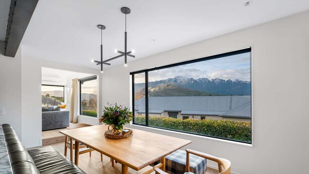 Un comedor moderno con una mesa y sillas de madera, un banco y un amplio ventanal con vistas a montañas y un lago.
