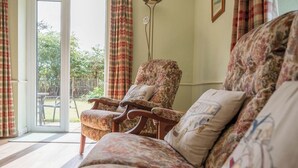 A living room with a sofa and armchair, a floor lamp, and a view of the outdoors through a glass door. - Mount Pleasant Farm, Dunwich (Dunwich)