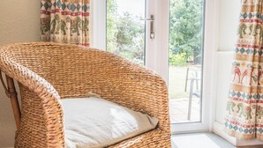 A wicker chair with a cushion in a room with a glass door leading to an outdoor area. - Mount Pleasant Farm, Dunwich (Dunwich)