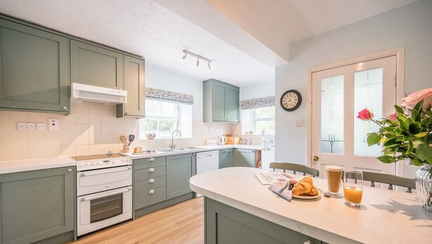 A kitchen with light green cabinets, a white countertop, and a dining area with a table set for breakfast. - Mount Pleasant Farm, Dunwich (Dunwich)