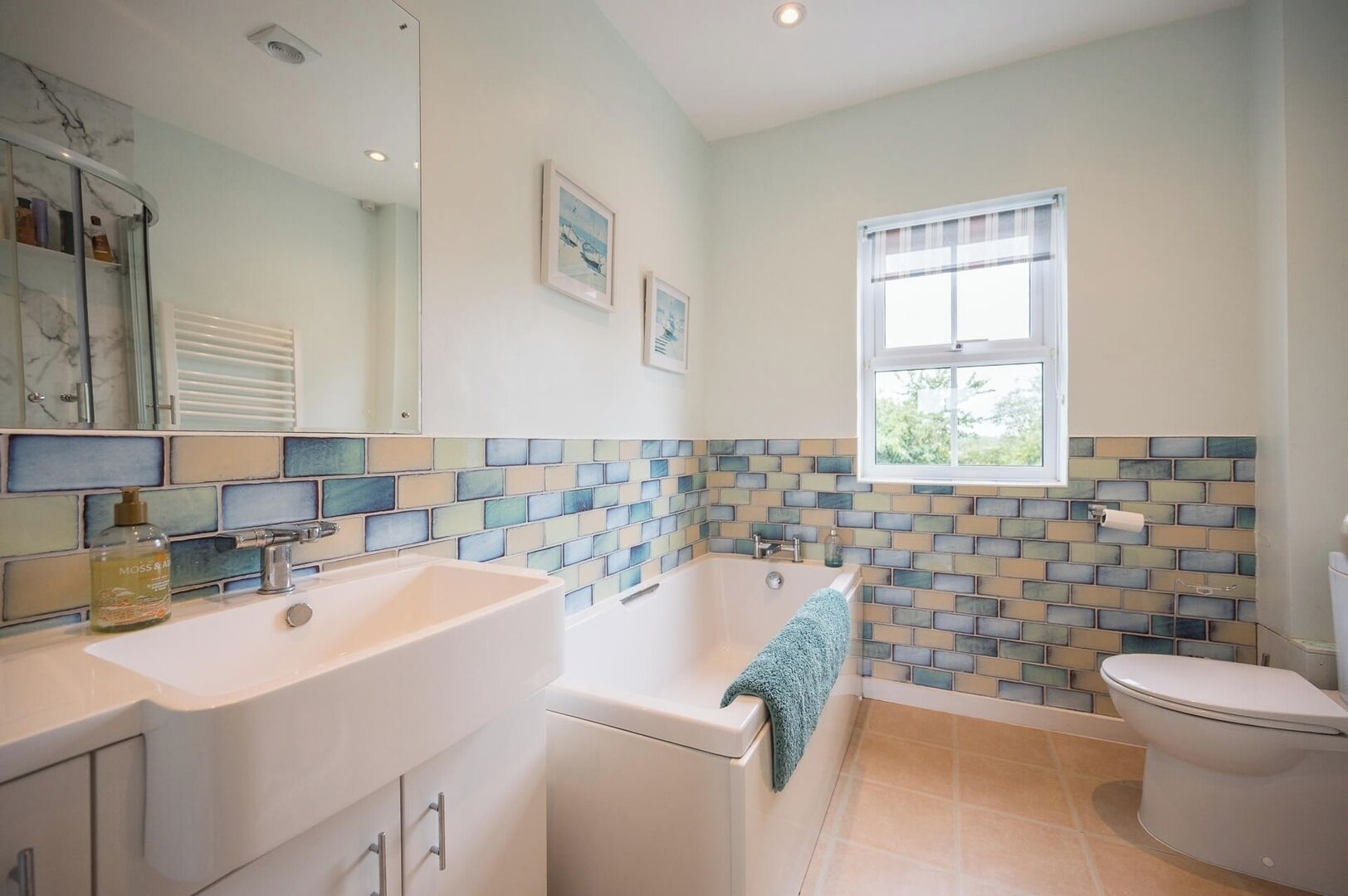 A modern bathroom with a large sink, a bathtub, and a toilet. There is a window providing natural light and a tiled backsplash.