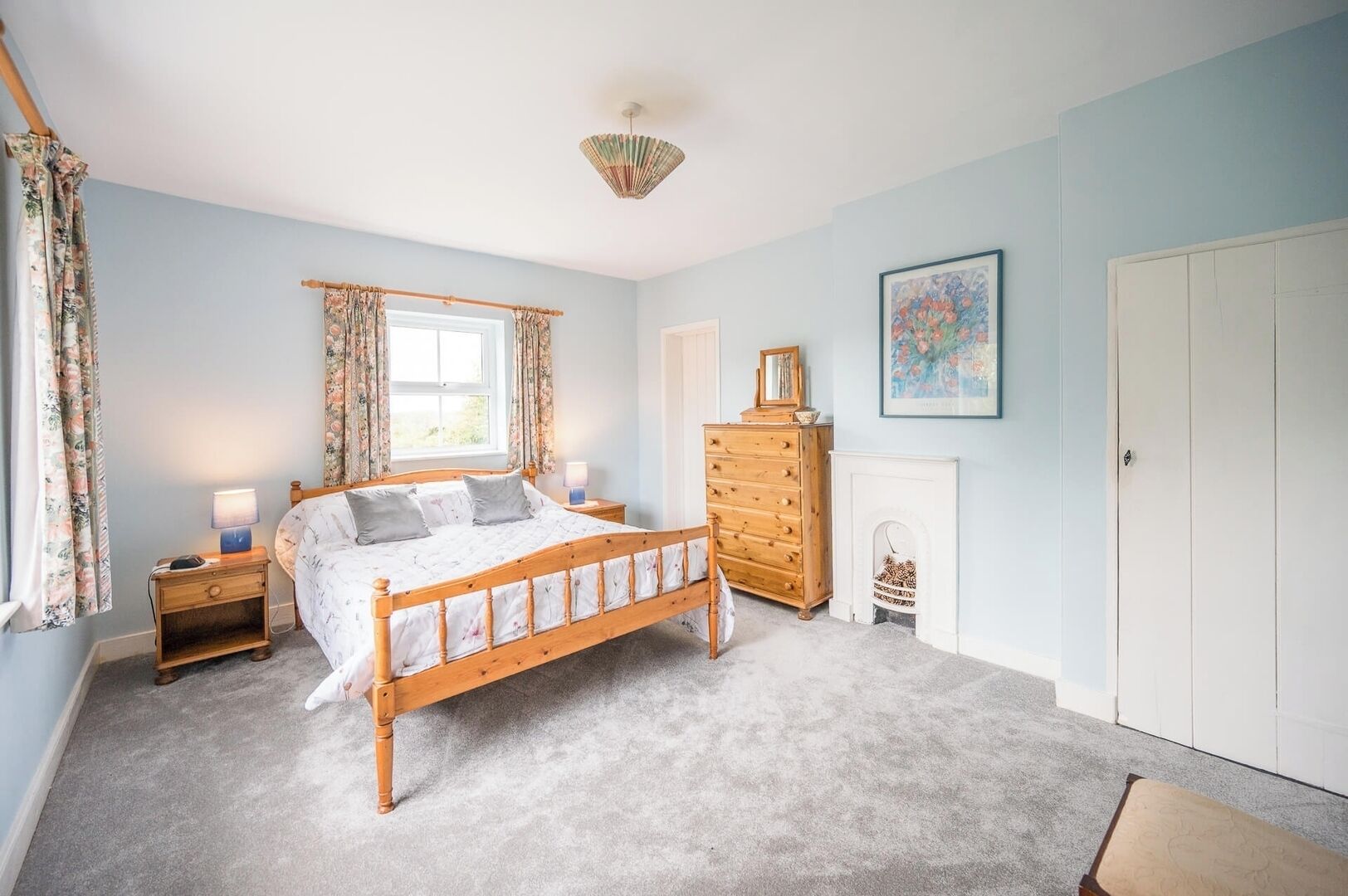 Une chambre à coucher avec un lit en bois, une commode, une table de chevet, une lampe, une cheminée et une porte.