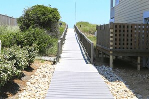 A wooden boardwalk leading to a building with a wooden fence on one side. - Whispering Waves - 5 BR Oceanside Home in Duck w/Private Pool, Dogs Allowed (Duck)