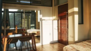 A room with a bed, a dining table with chairs, a sliding glass door to a balcony, and a wooden door. - Charming 5-bedroom Villa in Baguio with Heated Dipping Pool :Glass & Green Perch (Baguio)