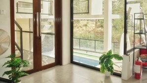 A modern interior with a glass door leading to a balcony, a potted plant, and a fire extinguisher. - Charming 5-bedroom Villa in Baguio with Heated Dipping Pool :Glass & Green Perch (Baguio)