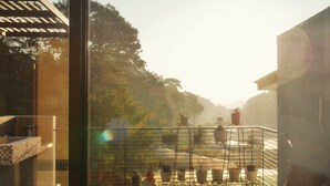 A balcony with potted plants, a metal railing, and a view of trees and a building. - Charming 5-bedroom Villa in Baguio with Heated Dipping Pool :Glass & Green Perch (Baguio)