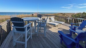 A wooden deck with Adirondack chairs and a table, overlooking a beach with a clear sky. - Kohler Cottage - 4 BR Oceanfront Cottage in Southern Shores w/Elevator (Southern Shores)