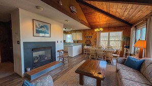 A cozy living room with a fireplace, wooden furniture, and a dining area with chairs and a table. - Kohler Cottage - 4 BR Oceanfront Cottage in Southern Shores w/Elevator (Southern Shores)
